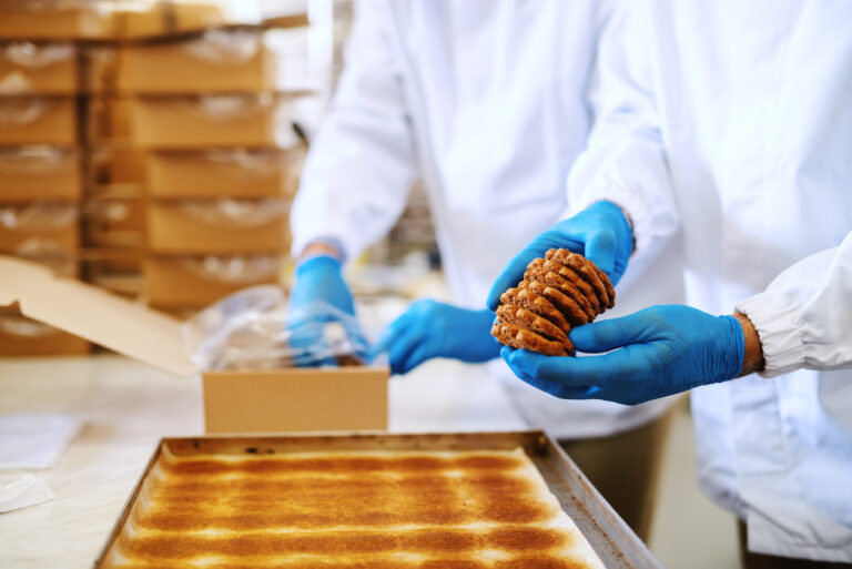 bakery assembly line workers packaging cookies wearing blue gloves
