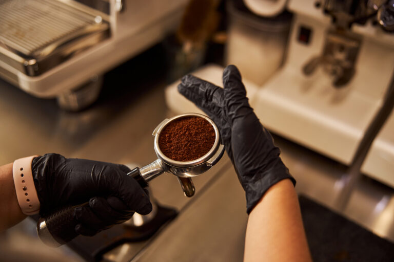 gloved hands filling an espresso machine cup