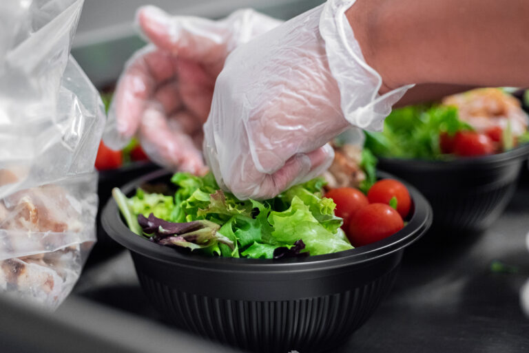 Gloved hands prepping a salad to-go