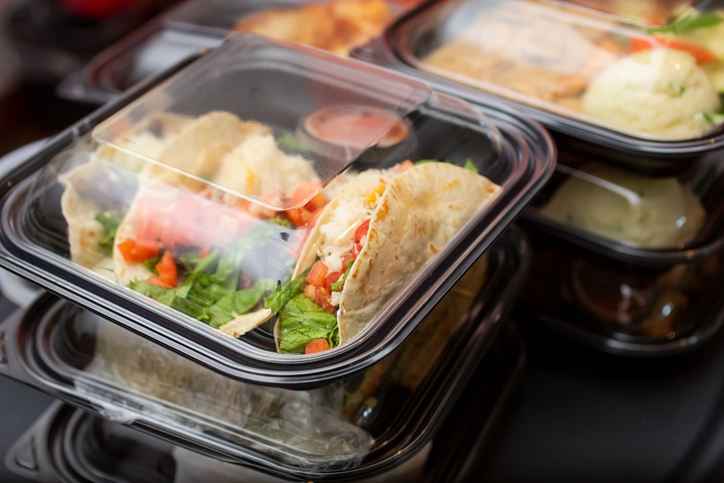 A view of several entrees prepared inside to-go plastic containers, ready for take-out orders, in a restaurant setting.