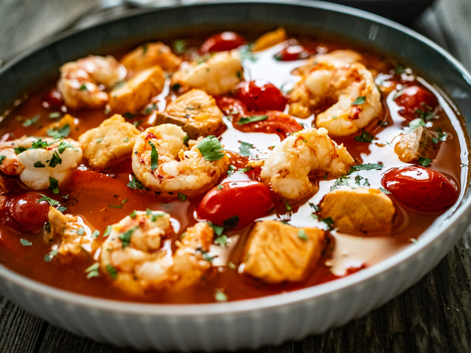 Fish soup with prawns and tomatoes on wooden table