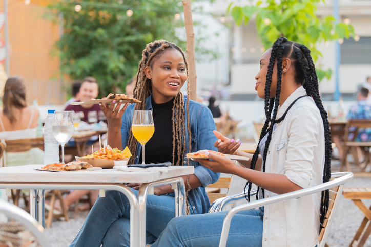 Smiling afro american women enjoying food and drinks at an outdoors terrace on an out of focus background. Selective focus: Friendship concept.
