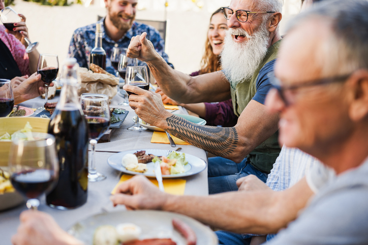 Family people eating at barbecue dinner outdoor - Focus on senior hand holding glass of wine