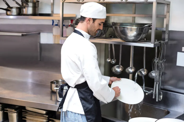 Handsome employee doing dishes in commercial kitchen. Order with a foodservice equipment buying group