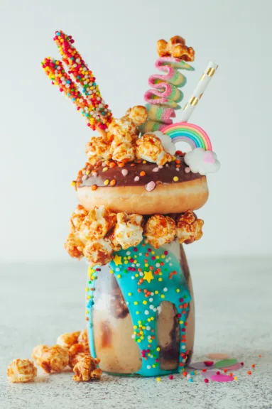 Chocolate freak shake topping with donut and caramel popcorn with sweets and straw; selective focus.