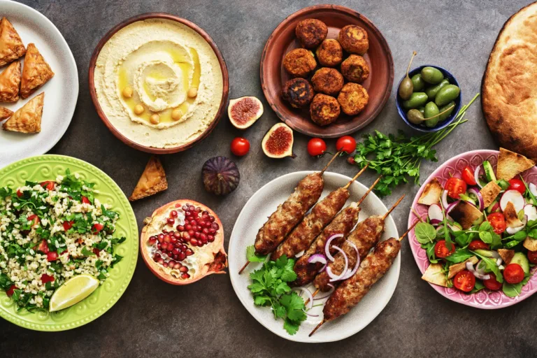 Arabic and Middle Eastern dinner table. Hummus, tabbouleh salad, Fattoush salad, pita, meat kebab, falafel, baklava, pomegranate. Set of Arabian dishes. Top view, flat lay.